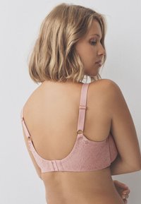 Soutien-gorge en dentelle rose avec bretelles ajustables, détails à motif floral, texture lisse et fermeture dos à agrafes.
