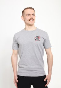 Šedé tričko s krátkým rukávem, které má na hrudi barevnou grafiku s textem a výrazným designem, vyrobené z měkké tkaniny.