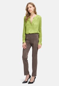 Blusa di seta verde con scollatura a V, abbinata a pantaloni in suede grigi. Le calzature presentano tacchi neri appuntiti. Elementi di design semplici e sartoriali.