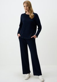 Navy knit sweater and matching wide-leg pants. Textured fabric, crew neckline, and side pockets. Paired with white sneakers.