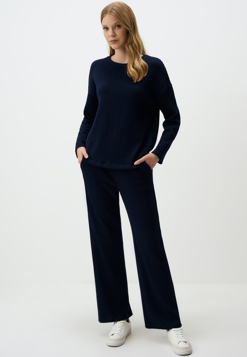 Navy knit sweater and matching wide-leg pants. Textured fabric, crew neckline, and side pockets. Paired with white sneakers.