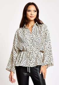 White shirt with black spotted pattern, buttoned front, long sleeves, peplum waist with drawstring, paired with black leather pants.