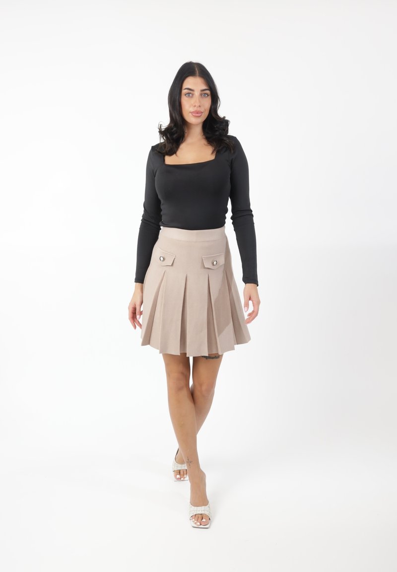 Falda plisada beige con dos bolsillos delanteros y botones de metal, combinada con una camiseta de manga larga negra ajustada. Fondo claro.