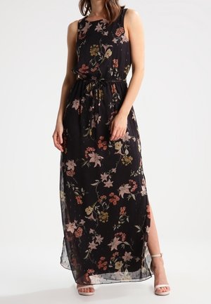 Robe longue noire avec imprimé floral en rose et vert. Tissu léger, sans manches avec une taille cintrée et une fente latérale, portée avec des talons clairs.