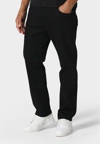 Pantalones de mezclilla negros con corte recto, con bolsillos laterales y un ligero estiramiento. Llevados con zapatillas blancas, sobre un fondo neutro.