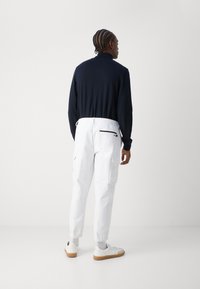 Ναυτικό μπλουζάκι με μακριά μανίκια συνδυασμένο με λευκά cargo παντελόνια που διαθέτουν ελαστική μέση, τσέπες και διακριτική σήμανση. Λευκά παπούτσια ολοκληρώνουν το σύνολο.