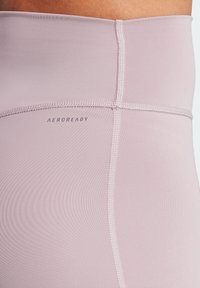 Světle růžové sportovní legíny s hladkou texturou, s kontrastním šitím a logem "AEROREADY" na pase.