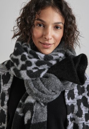 Soft, black and grey leopard print scarf with a fuzzy texture, wrapped around the neck, featuring a knitted design and contrasting patterns.