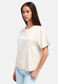 Μπεζ βαμβακερό T-shirt με κοντά μανίκια, με λευκό αφηρημένο σχέδιο και κείμενο στο μπροστινό μέρος. Στρογγυλός λαιμός και άνετη εφαρμογή.