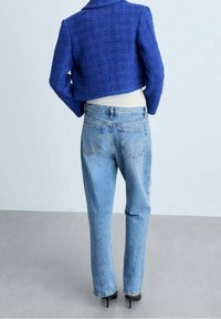 Giacca blu in tessuto testurizzato con revers ampi, abbinata a jeans a gamba dritta blu chiaro e scarpe con tacco nere.