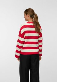 Maglione a righe rosse e crema con vestibilità morbida, scollo a costine e maniche lunghe, indossato con pantaloni scuri, che mostrano una trama a maglia liscia.