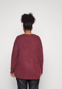 Übergroßer burgunderfarbener Pullover mit langen Ärmeln, überschnittenen Schultern und strukturiertem Strick; getragen über schwarzen Lederhosen.