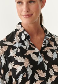 Black button-up shirt featuring a floral leaf pattern in light pink and blue. Smooth fabric with a classic collar and a relaxed fit.