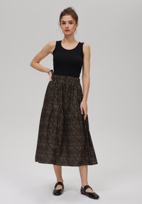 Svart linne med rund halsringning, som kombineras med en lång, utsvängd kjol med ett brunt prickigt mönster. Svarta lägenheter fulländar outfiten.