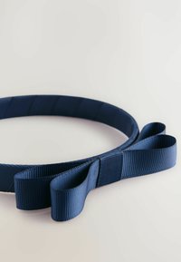 Granatowa opaska do włosów z kokardką, spoczywająca na jasnym tle, z teksturowanym wzorem wstążki.