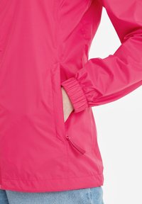 Pink waterproof jacket with elastic cuffs, side pockets, and a zip pull detail. The fabric has a smooth, glossy texture.