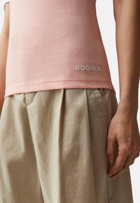 Světle růžový přiléhavý top s logem "BOGNER", doplněný volnou béžovou skládací sukní. Tkanina vypadá jemně a lehce.