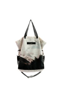 Bolsa de lona con estampado de montaña y bosque, correa de hombro desmontable en blanco y negro, y asas negras con texto en blanco.