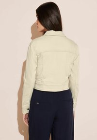 Avskuren, ljusbeige denimjacka med krage, långärmar och knappdetaljer. Matchas med mörknavy byxor.