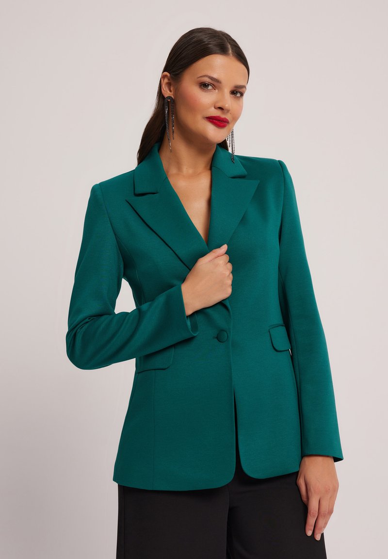 Błękitny żakiet o dopasowanym kroju, z klapami i dwiema przednimi kieszeniami. Gładka faktura oraz zapięcie na jeden guzik dodają charakteru.