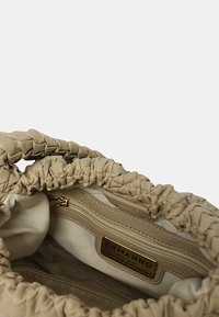 Borsa beige con design in tessuto arricciato, texture simile alla pelle e etichetta del marchio in rilievo dorata. Presenta una tasca interna con zip.