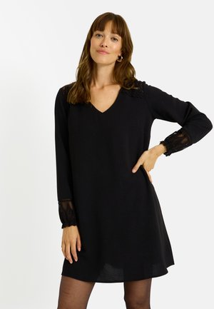 Robe noire avec un décolleté en V, manches longues avec des accents en dentelle, texture douce, coupe décontractée et ourlet qui tombe au-dessus du genou.