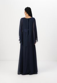 Navy blue floor-length dress with sheer cape sleeves, detailed with sequins at the back, featuring a round neckline and zip closure.