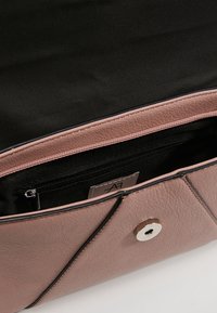 Hnědá kožená kabelka s magnetickým zapínáním, otevřená, ukazuje černou látkovou vnitřní část a zipovou kapsu uvnitř s štítkem.