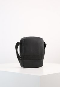 Borsa a tracolla in pelle nera con chiusura a zip, banda in tessuto testurizzato e tracolla regolabile, caratterizzata da una forma cilindrica e un design compatto.