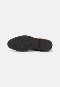 Pantof brown din piele cu o talpă din cauciuc negru texturat, având un model geometric și un design superior neted.