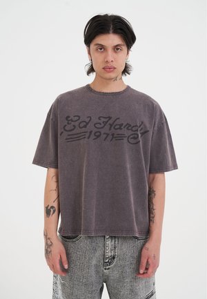 Grijze oversized T-shirt met vervaagde afwerking, met "Ed Hardy 1971" in zwart cursief gedrukt op de borst. Korte mouwen en ronde hals.