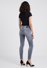 Jeans gris ajustados con cintura alta, bolsillos traseros y detalles de costura sutiles, combinados con stilettos negros y una camiseta negra.