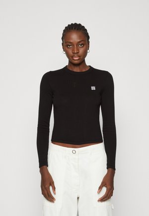 Svart langt ermet ribbet crop topp med rund hals og lite hvitt logo på venstre side, kombinert med hvite cargo bukser.