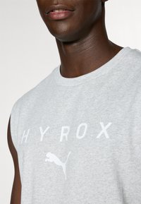 Grå ermeløs t-skjorte laget av bomullsblanding, med iøynefallende hvit "HYROX"-tekst og en hvit Puma-logo, rund halsutringning og glattekstur.