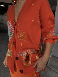 Cardigã laranja tricotado com bordados de flores e frutas. Apresenta botões grandes e um design de decote V profundo. Ajuste oversized confortável.