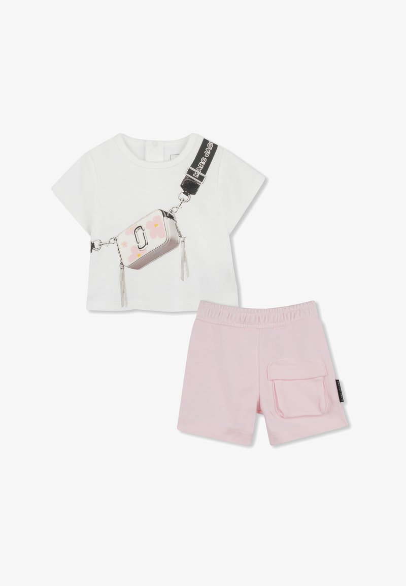 Camicia bianca a maniche corte con una grafica di una borsa con accenti floreali. Pantaloni corti rosa chiaro con cinturino elastico e tasca laterale.