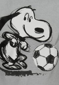 Camiseta gris con un perrito de dibujos animados en tinta negra, sonriendo y jugando con un balón de fútbol en blanco y negro. Líneas simples y diseño audaz.
