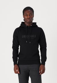 Sudadera negra con capucha y bolsillo frontal. Logo "Originals" impreso en un acabado mate oscuro. Textura de tela simple y suave.