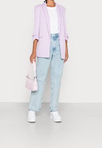 Jasnofioletowa, przewymiarowana marynarka, biała koszulka, jasnoniebieskie dżinsy z wysokim stanem i białe, masywne sneakersy. Mała różowa torebka na pasek.