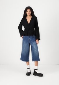 Must mustvalge särk sügava V-kaelusega ja sidumisega detailidega, koos laia säärega helesiniste denim-kaltsooga ning mustade platvormkingadega.