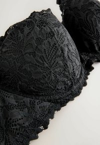 Sort blonde-bh med intrikate blomsterdesigns, bølgede kanter og glatte skåle. Materialet har en delikat, struktureret overflade.
