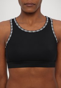 Black sports bra with wide straps featuring white logo accents along the neckline. Smooth, stretchy fabric with a fitted design.