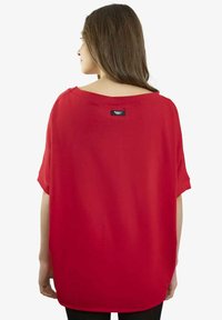 Czerwona luźna bluzka z krótkimi rękawami, okrągłym dekoltem i zakrzywionym dołem. Miękki materiał z małą metką marki z tyłu.