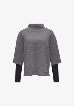 Schwarz-weiß gestreiftes Oberteil im Hahnentrittmuster mit hohem Kragen, abgesenkten Schultern und Dreiviertelärmeln, das eine einfarbige schwarze Unterlage hat.