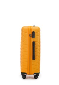 Valise rigide de couleur jaune vif avec une surface texturée, dotée d'une fermeture éclair et d'une poignée noires, ainsi que de quatre roulettes pivotantes pour une meilleure mobilité.