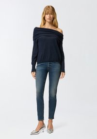 Mornarica off-shoulder pletena pamučna majica, rebrasta tekstura, u kombinaciji sa uskim izblijedjelim plavim farmerkama i srebrnim cipelama s šiljastim prstima i dekorativnim detaljima.