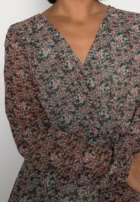 Růžový šaty s květinovým potiskem a dlouhými rukávy. Mají výstřih do V, lehký materiál a kombinaci zelené, červené a hnědé barvy.