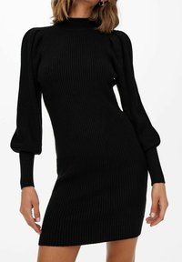 Robe en maille côtelée noire avec un col montant, une silhouette ajustée et des manches bouffantes. Texture douce et longueur au-dessus du genou.