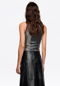Srebrny top na cienkich ramiączkach zdobiony cekinami, o dopasowanym kroju, zestawiony z wysokim stanem czarnej skóry, charakteryzującej się gładką fakturą i prostymi liniami.
