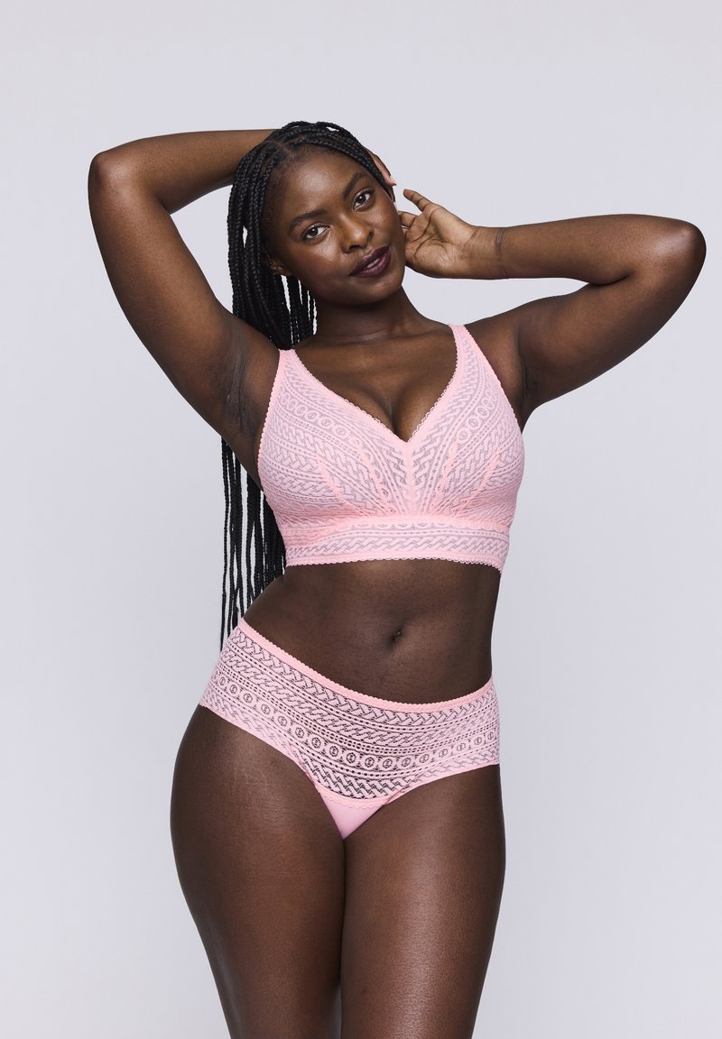 Vaaleanpunainen pitsinen bralette V-dekoltee-muotoilulla ja siihen sopivat pitsireunaiset alushousut. Yksityiskohdat ovat huolellisesti tehtyjä ja materiaali on sileä.